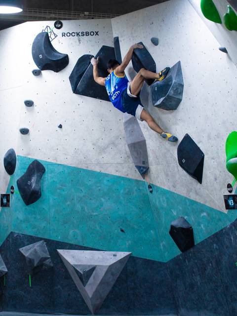 Un tipo está subiendo en un muro de escalada indoor en un gimnasio.
