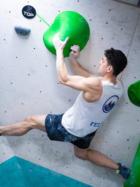 Un escalador está intentando alcanzar una presa verde en un muro de escalada interior.