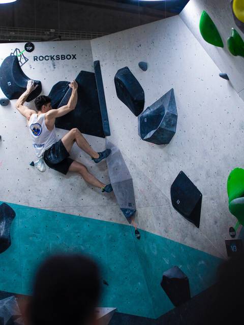 Un escalador desafiando una pared de boulder en un gimnasio de escalada.