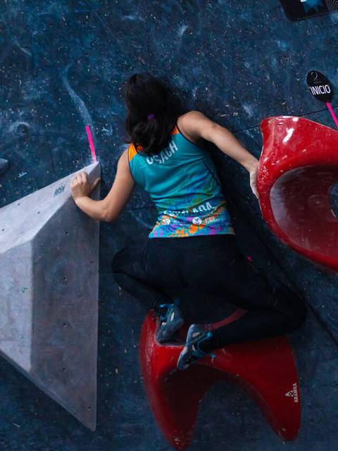 Una escaladora se enfrenta a un bloque de escalada desafiador en un gimnasio.