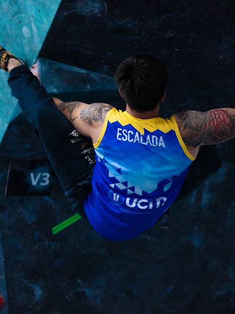 Un escalador con un tatuaje destacado está realizando una ruta de boulder en una competencia.
