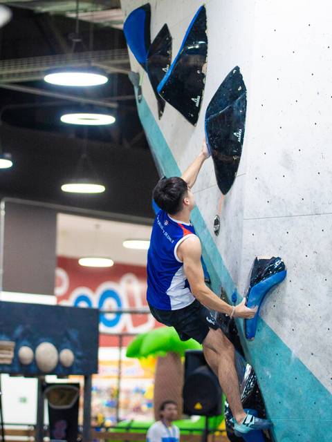 Un escalador está haciendo boulder en una pared de escalada indoor.