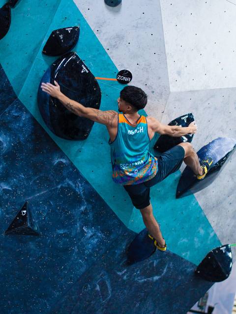 Un escalador se enfrenta a una pared de boulder en una competencia.