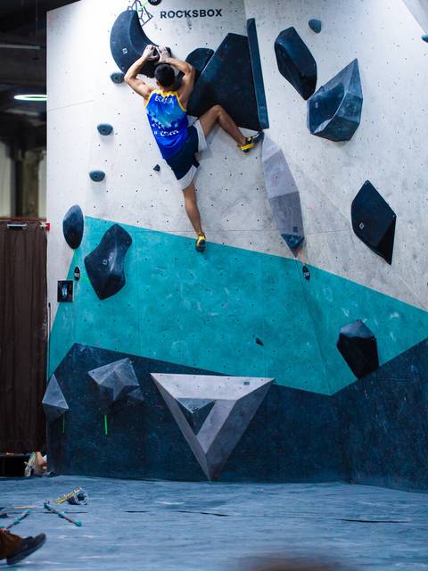 Un escalador está desafiando una pared de boulder en una competencia indoor.