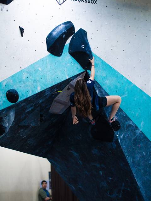 Una persona está escalando en una pared de boulder en un gimnasio.
