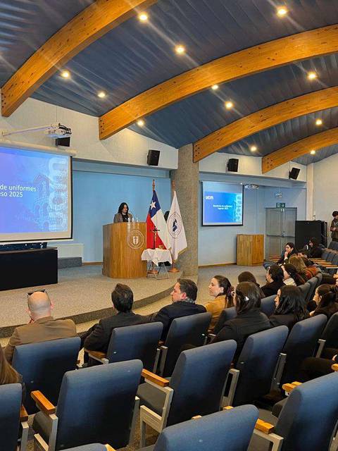 Una ceremonia de graduación con estudiantes y un presentador en un auditorio.