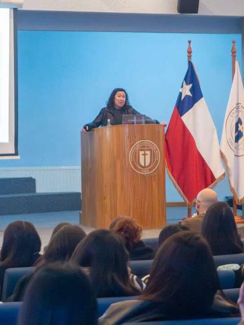Una exposición académica en una sala con gente atenta y banderas chilenas.
