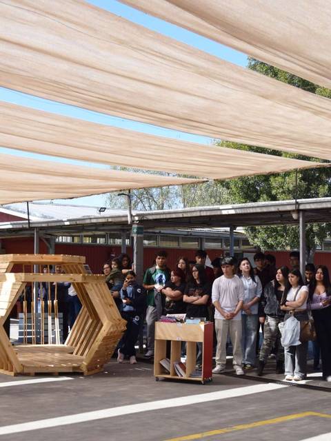 Un grupo de estudiantes escucha a un orador bajo un toldo en un espacio abierto.