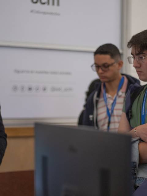 Un grupo de jóvenes escucha atentamente a un profesor mientras le muestra una presentación en una computadora.