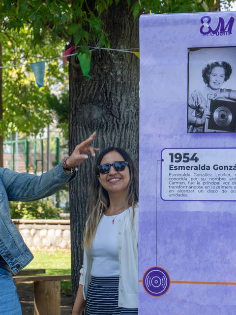 Un par de mujeres están junto a una estructura que muestra una foto histórica en un evento al aire libre.
