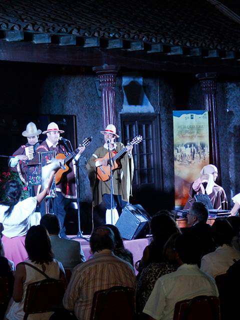 Un grupo de personas está realizando una presentación musical en un escenario con un público atento.