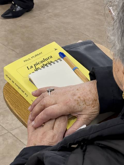 Una señora mayor sostiene un libro titulado 'La picadura de la alacrana' sobre una mesa.