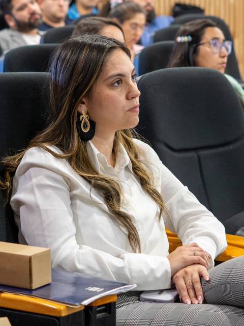 Una mujer atenta en un evento, escuchando a los expositores con interés.