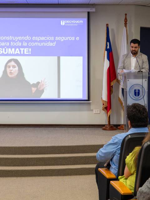 Un presentador habla en una conferencia en la UCM, mientras una imagen se proyecta detrás de él.