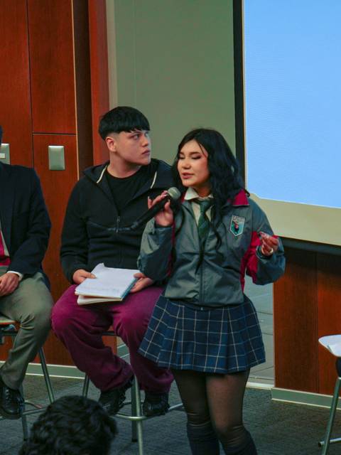 Un grupo de estudiantes participa en una discusión en un panel frente a un público atento.