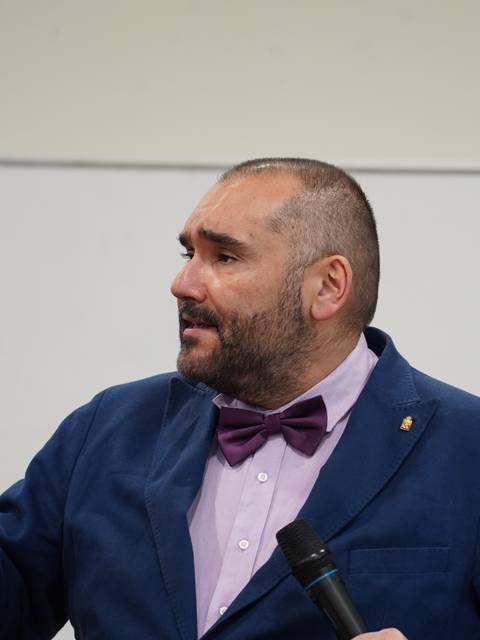 Un hombre con chaqueta azul y pajarita que está hablando en un evento.