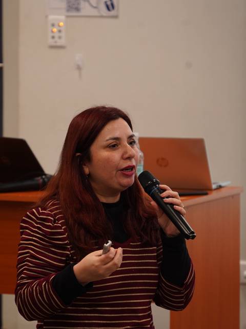 Una mujer expone con entusiasmo en un seminario mientras sostiene un micrófono.