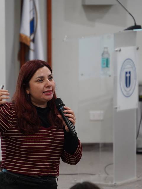 Una mujer con pelo rojo habla apasionadamente ante un público en una presentación.
