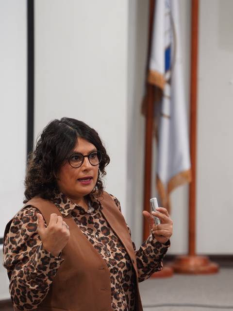 Una mujer con cabello rizado y gafas expone en un auditorio.