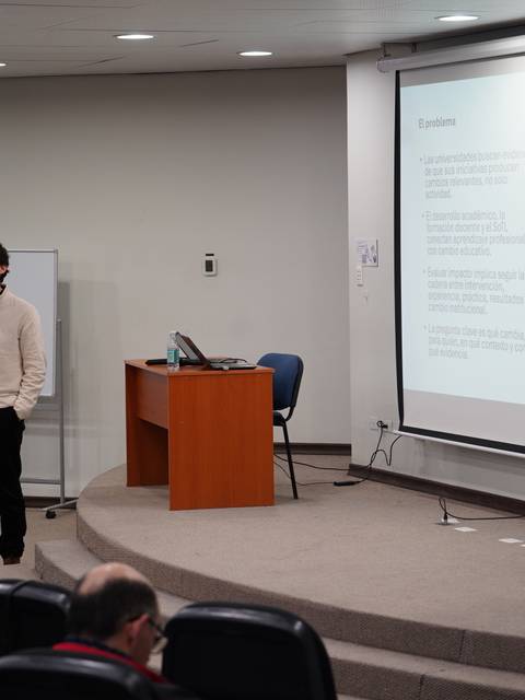 Un cabro expone en una charla mientras se proyectan diapositivas en una sala de clases.
