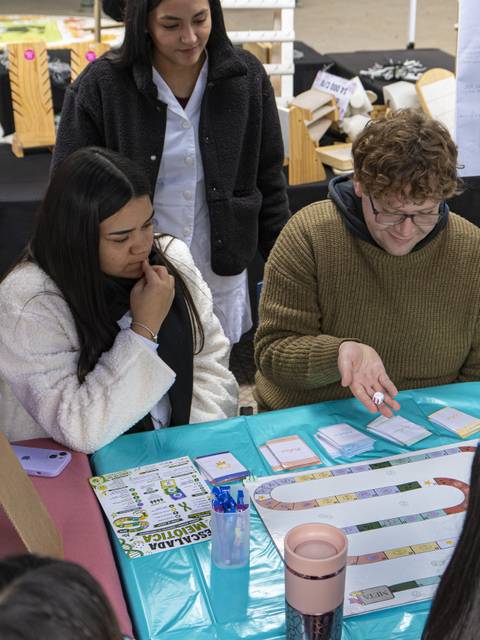 Un grupo de jóvenes se reúne para jugar un juego de mesa colaborativo en una feria escolar.