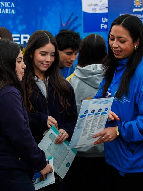 Un grupo de estudiantes interactúa en una feria educativa, recibiendo información sobre opciones académicas.
