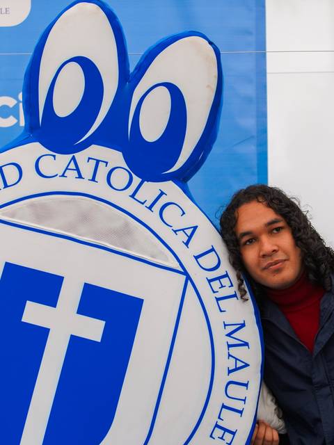 Un par de jóvenes posando junto a un letrero de la Universidad Católica del Maule.