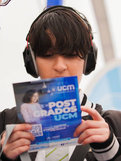 Un joven revisa un folleto de postgrados mientras escucha música con audífonos.