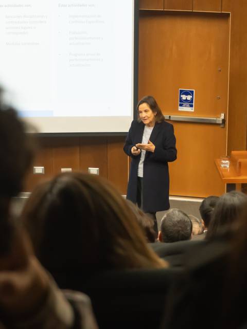 Una mujer se está presentando frente a una audiencia en una sala de conferencias.