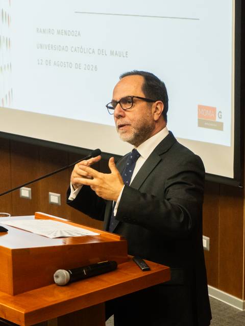 Un hombre está exponiendo en un seminario frente a una pantalla con información.