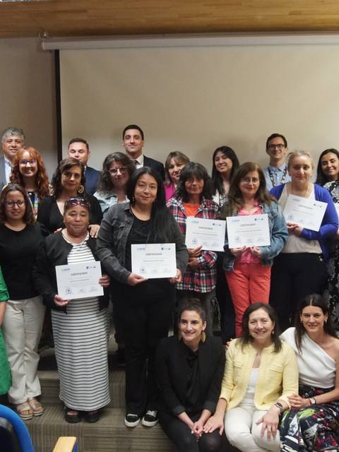 Un grupo diverso de personas posa emocionado con sus certificados en un evento de entrega en Chile.