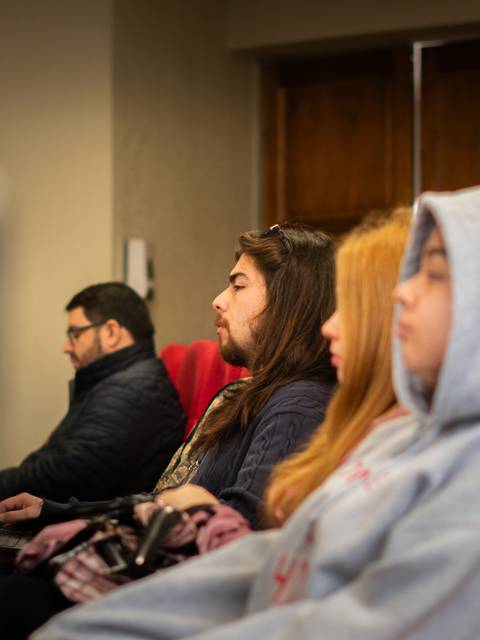 Un grupo de personas está sentada en sillas rojas, concentradas en lo que están mirando.