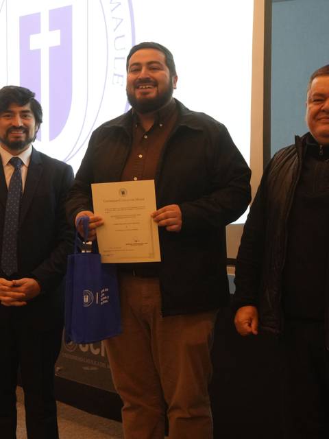 Tres hombres posan en un evento donde uno recibe un reconocimiento.