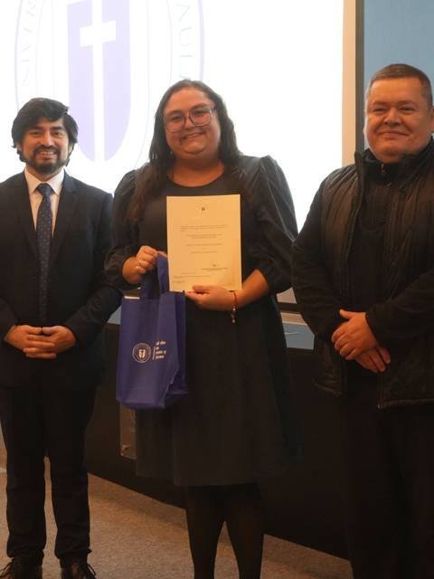 Tres personas posando en un evento de premiación en un auditorio.