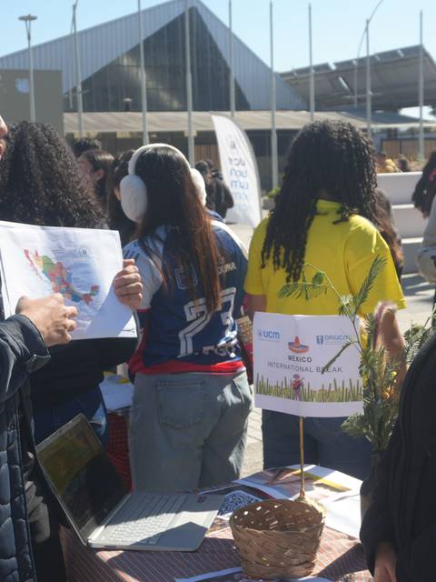 Un par de personas conversando en un evento al aire libre, con mapas y folletos en sus manos.