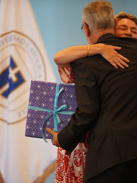 Una pareja se abraza emocionada en un evento mientras sostiene un regalo envuelto.