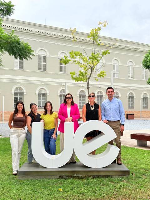 Un grupo de seis personas posando frente a una grande letra 'ue' en un espacio al aire libre.