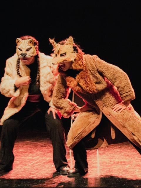 Dos actores con máscaras de animales y trajes llamativos realizan una actuación en el escenario.