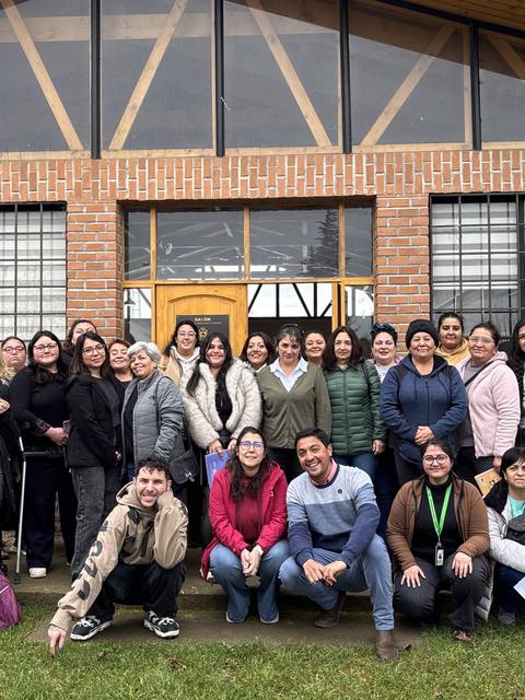 Un grupo de personas posando felices frente a un edificio en un día nublado.