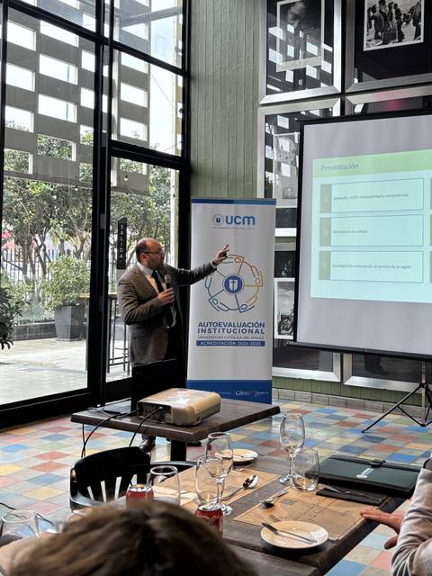 Un presentador expone información frente a un grupo en un ambiente acogedor.