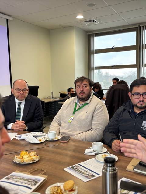 Un grupo de personas en una reunión con café y pasteles en la mesa.
