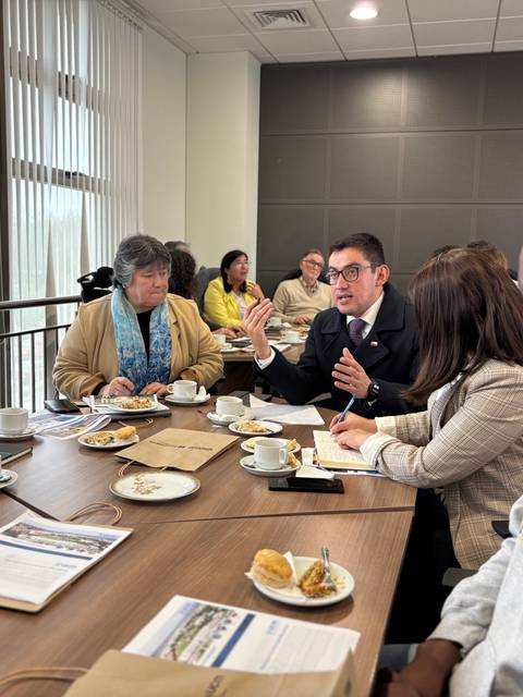 Un grupo de personas conversando en una reunión con café y bocadillos en la mesa.