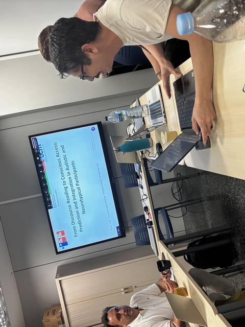 Un grupo de personas en una reunión en una sala con pantallas y laptops.