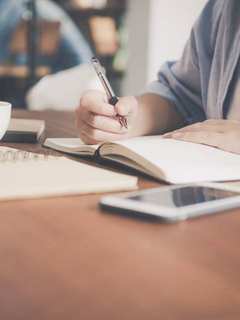 Una persona está escribiendo en un cuaderno mientras se toma un café.