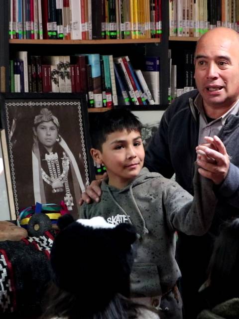 Un grupo de personas participan en una actividad educativa en una biblioteca, donde un hombre habla a un niño mientras otros lo observan.