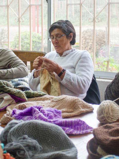 Un grupo de mujeres se reúne para tejer diferentes prendas en una mesa.