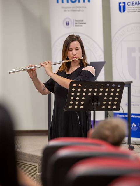 Una mujer está tocando la flauta en una presentación frente a una audiencia.