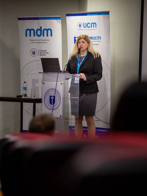 Una mujer presenta un tema en una conferencia frente a un público atento.