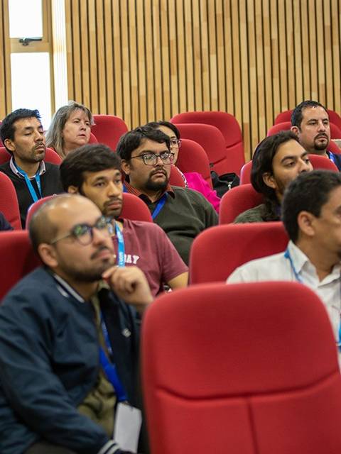 Un grupo de personas atentas en una charla en una sala con asientos rojos.
