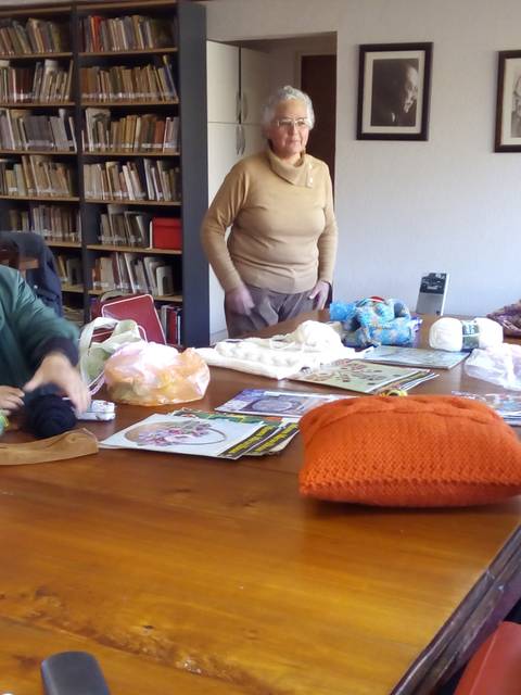 Un grupo de mujeres se reúne alrededor de una mesa, trabajando en proyectos de tejido y manualidades en un ambiente acogedor.